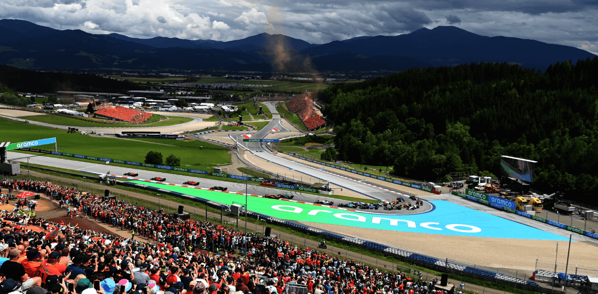 Drivers race through the scenic Red Bull Ring during the 2025 Austrian Grand Prix, surrounded by lush green hills and cheering fans.