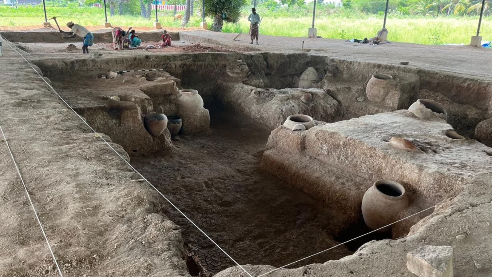 Keeladi excavation site with archaeologists uncovering brick structures near Vaigai River in Tamil Nadu.